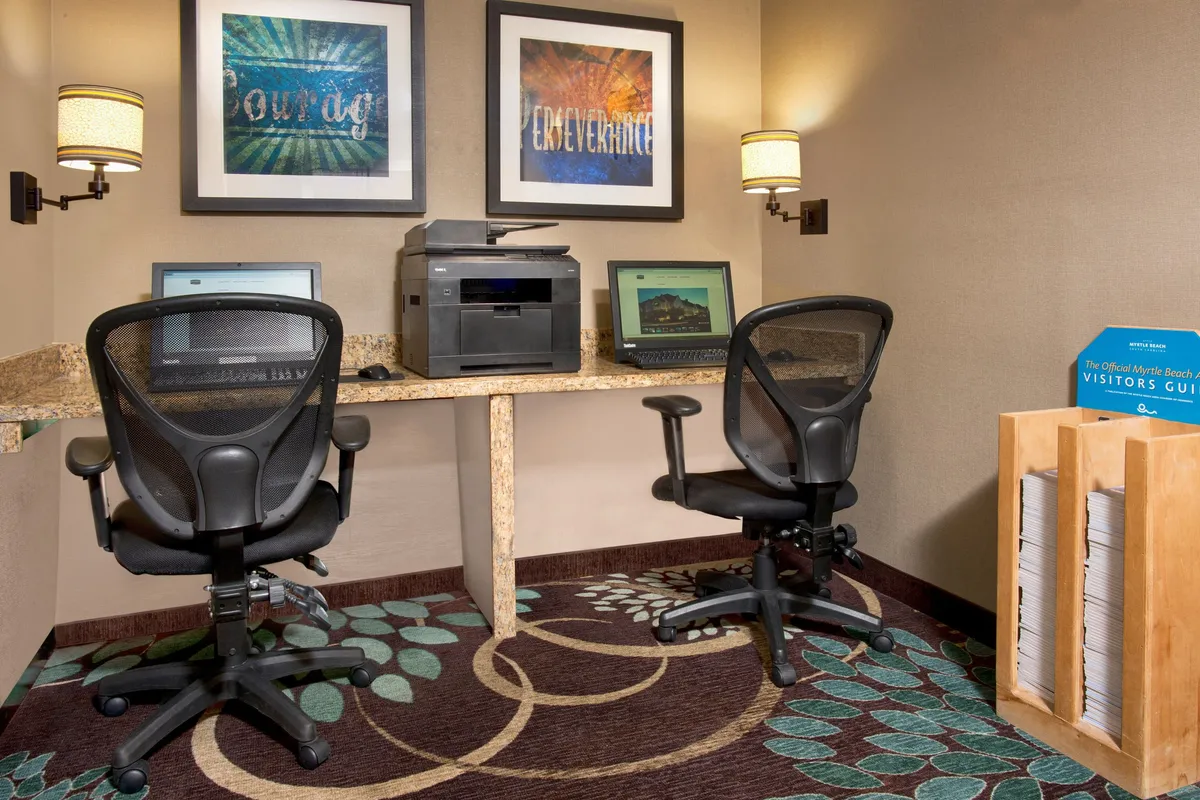 A functional business center with computer workstations, a printer, decorative wall art, and a rack of visitor guides, creating a productive yet welcoming environment for remote work or planning adventures.