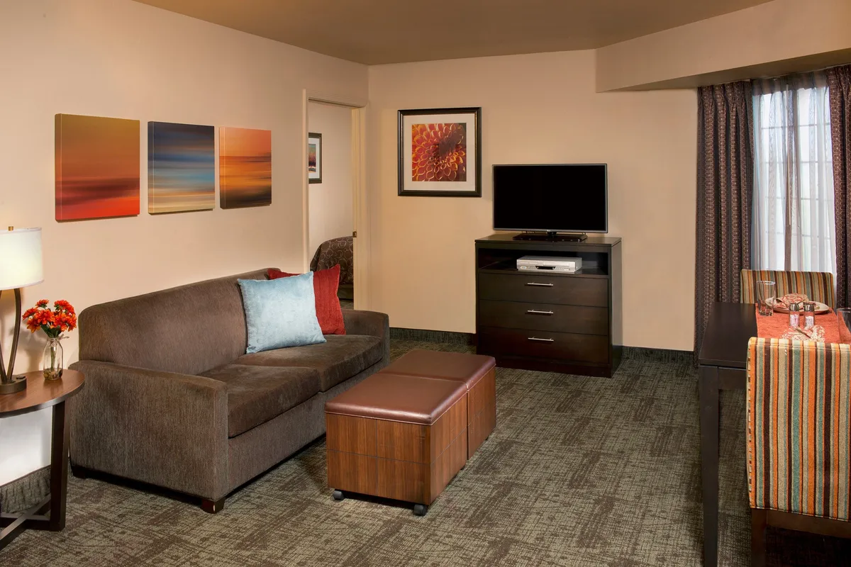 The image displays the inviting living room of the condo, featuring a plush sofa, vibrant artwork on the wall, a sleek television, and a coffee table set for relaxation or casual gatherings. The setting is warmly lit, creating a cozy and welcoming ambiance ideal for unwinding after a day of Myrtle Beach adventures.