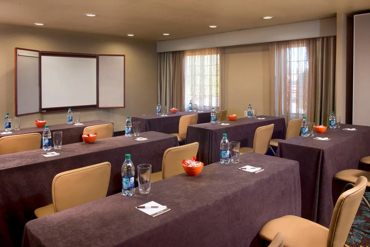 A collaborative table setting with wooden tables, water bottles, notepads, and snack bowls, arranged for business meetings or workshops. The mood is focused and social, suggesting opportunities for group planning or networking before heading out to local attractions.