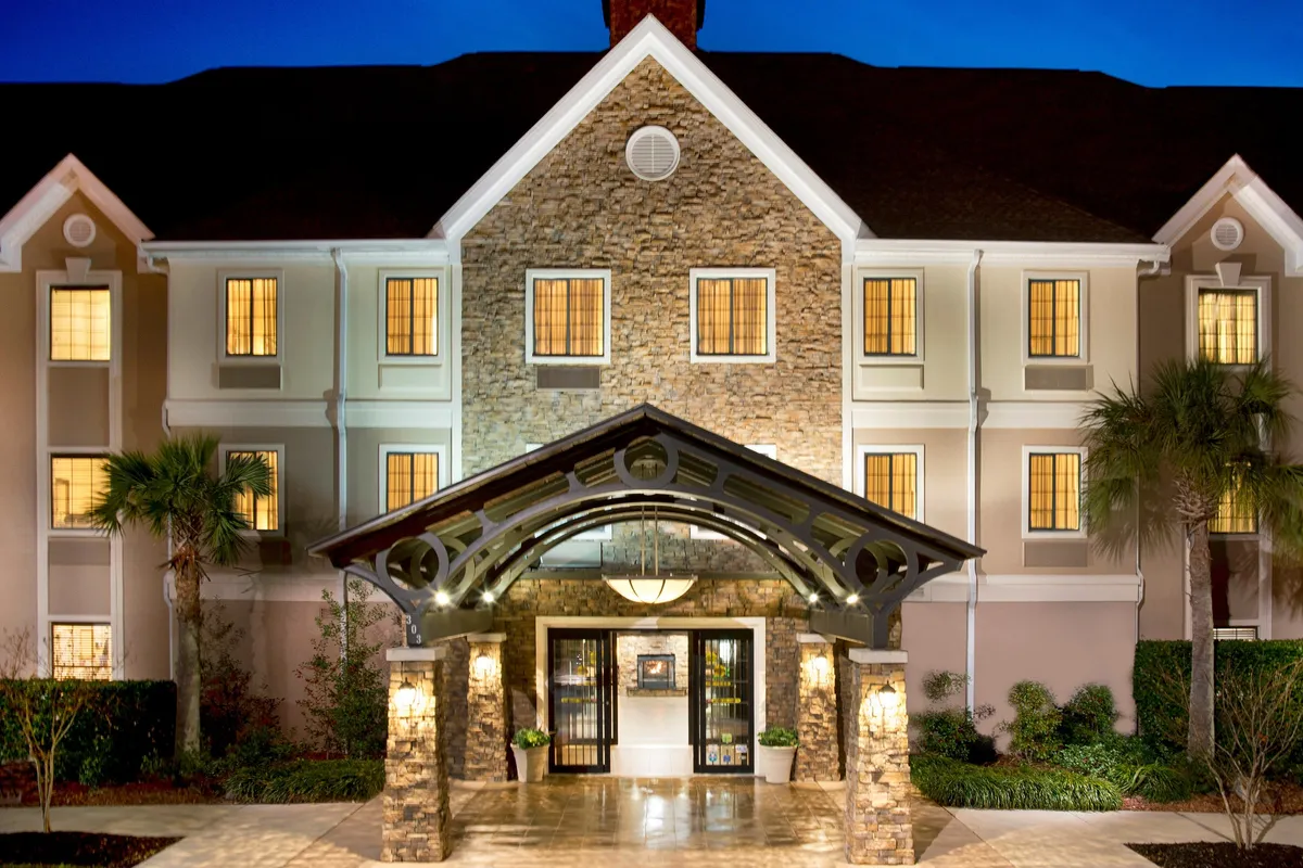 An inviting exterior view of the property's arched entrance with a stone facade and warmly lit windows. The entrance exudes a welcoming atmosphere, hinting at cozy evenings spent together and memorable arrivals. The lighting suggests an inviting ambiance for couples returning from a night out.