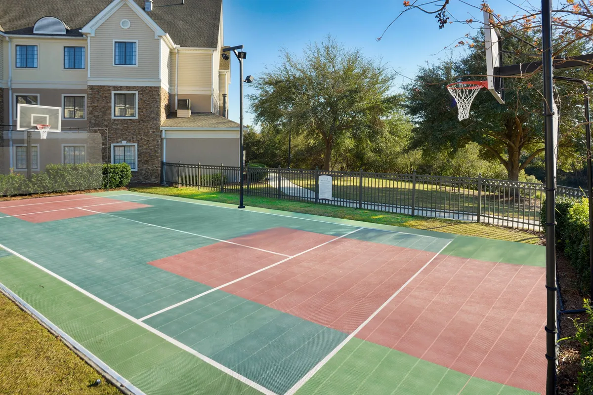 An energetic exterior view of a basketball court surrounded by lush greenery, with a clear focus on the basketball hoop and well-maintained court surface. The image radiates a lively and playful mood, suggesting opportunities for friendly games and social connection.