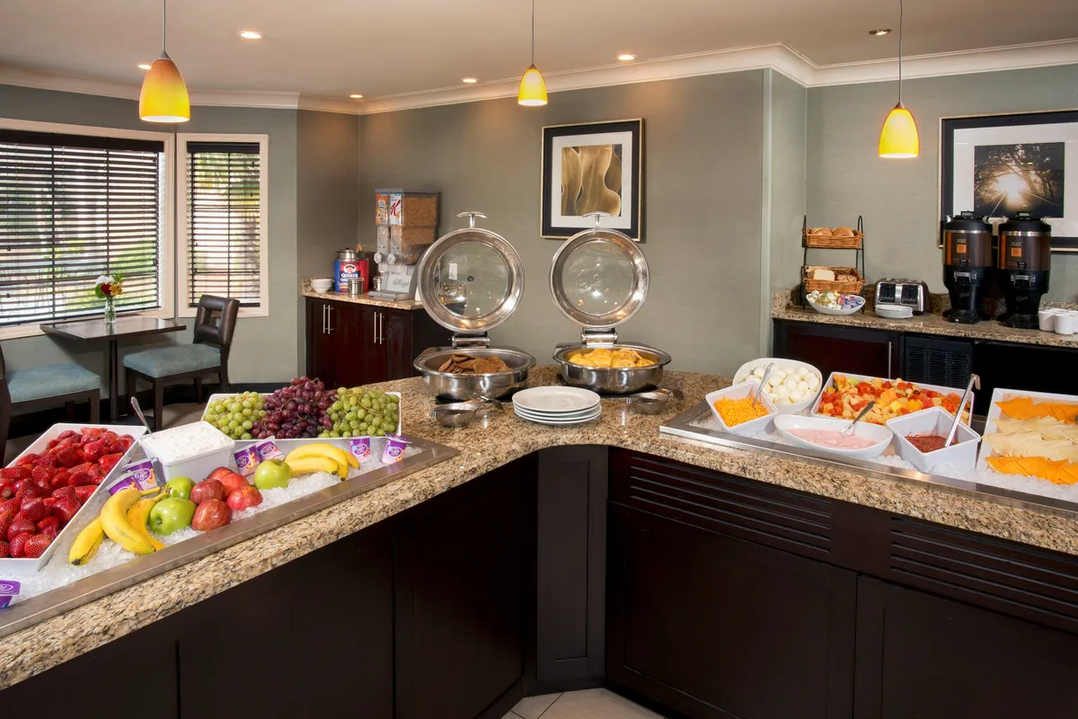 This image captures a buffet table set with an array of breakfast foods, a seating area inviting guests to gather, and decorative artwork that adds a cheerful ambiance. The layout suggests a communal dining experience, with fresh food easily accessible and ample space for socializing.