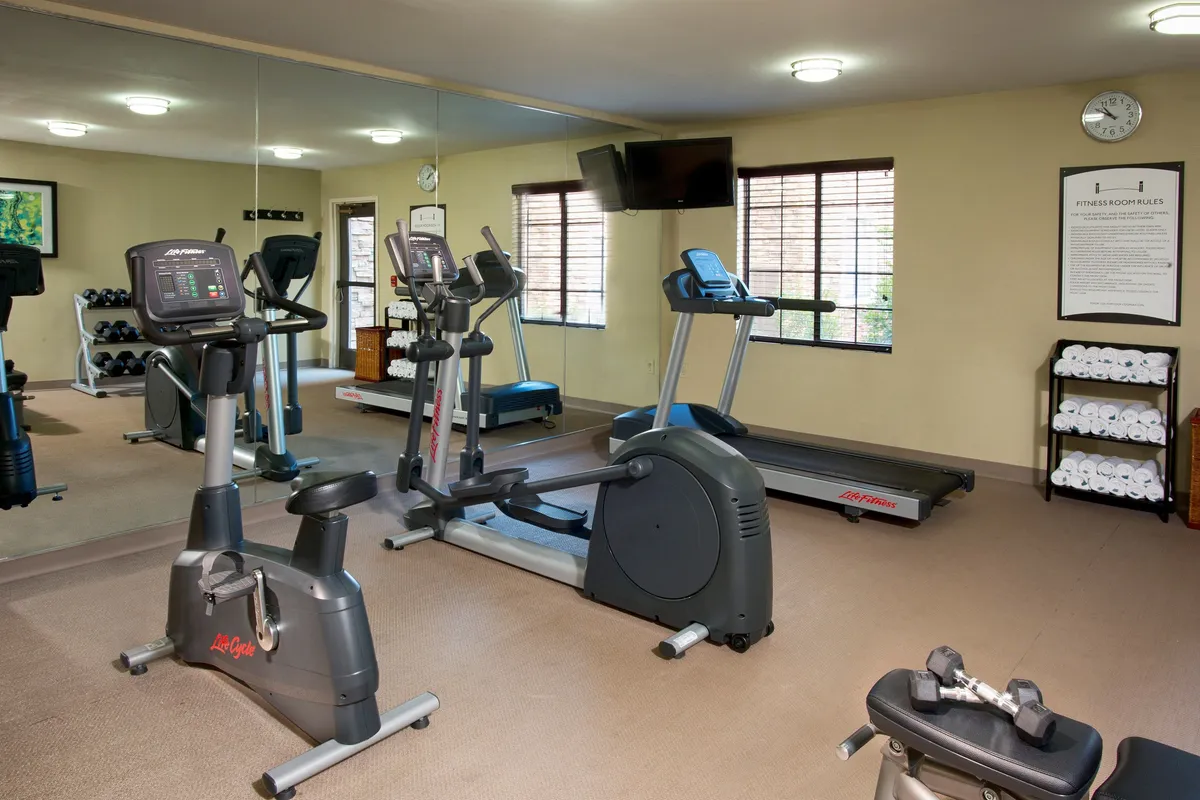A modern, well-equipped fitness center featuring exercise bikes, a treadmill, weights, large mirrors, and fresh towels. The space is bright and motivational, encouraging an active lifestyle.