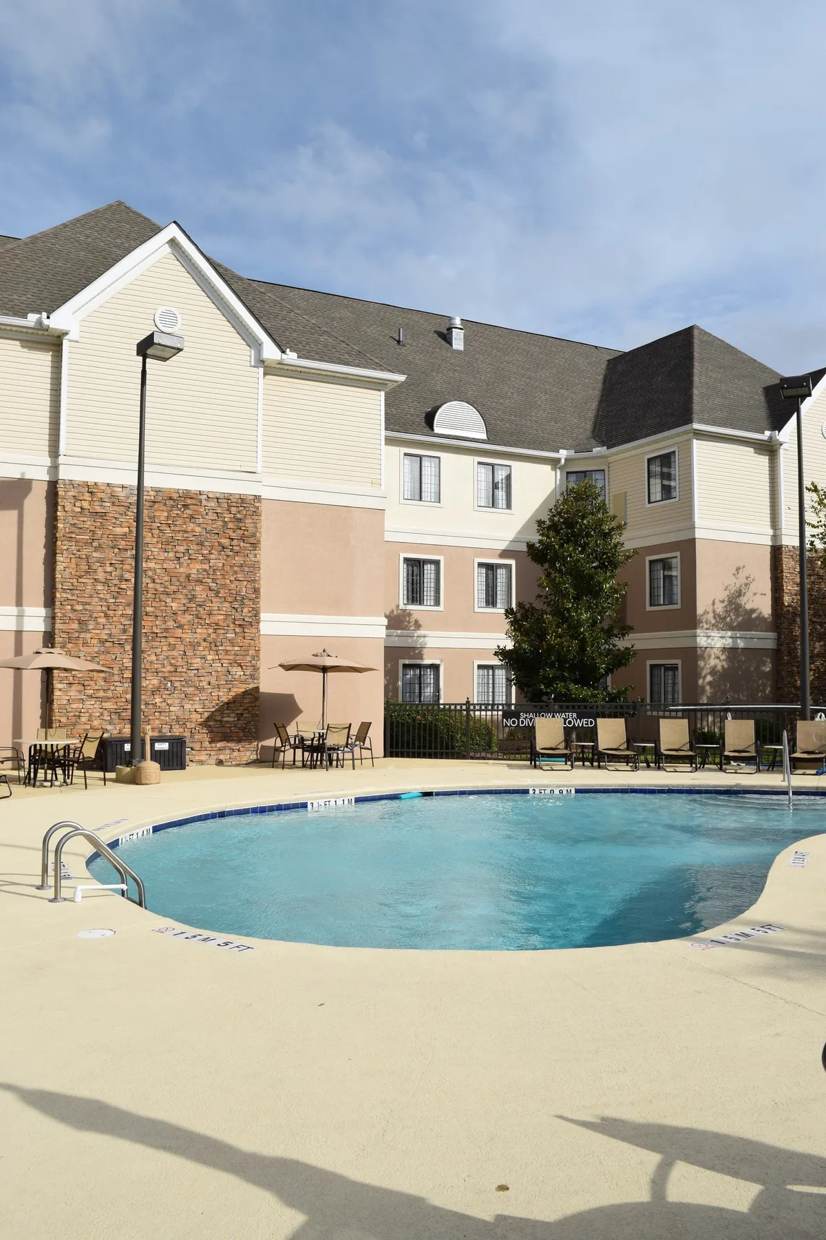 A serene exterior scene featuring a sparkling swimming pool surrounded by lounge chairs and manicured landscaping. The building's facade creates a welcoming backdrop, while the setting sun gives the scene a warm glow. Guests can be seen relaxing by the pool, suggesting a leisurely, romantic atmosphere.