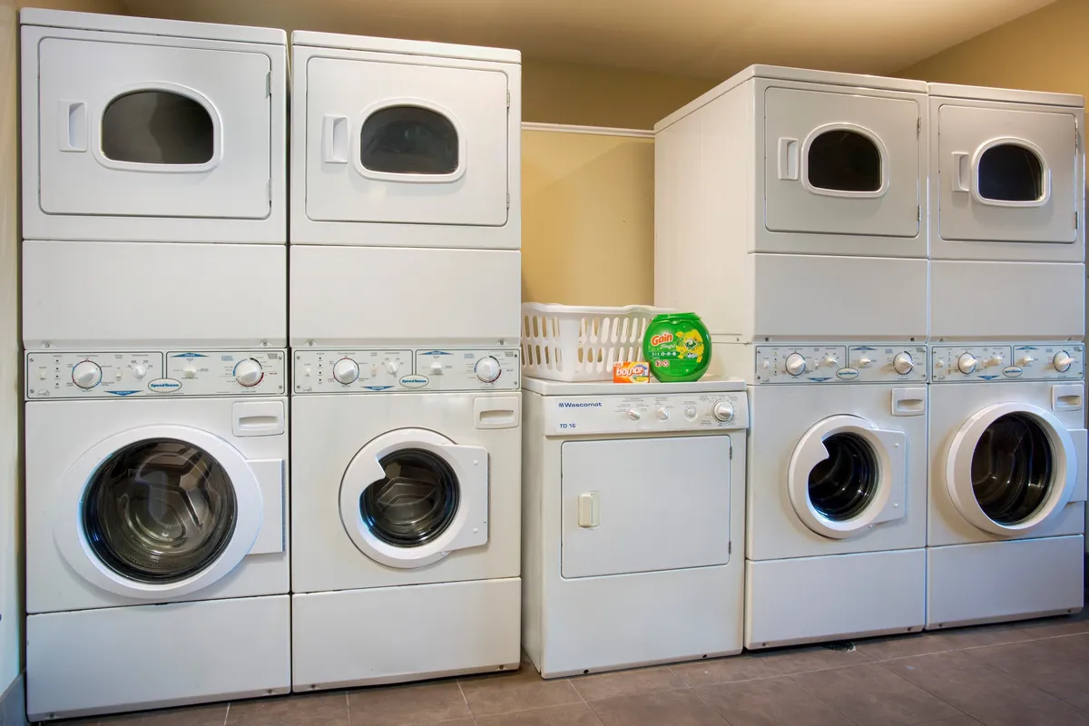 A practical laundry room with stacked washer and dryer units, a laundry basket, and detergent, offering guests the ability to refresh their clothes during their stay.