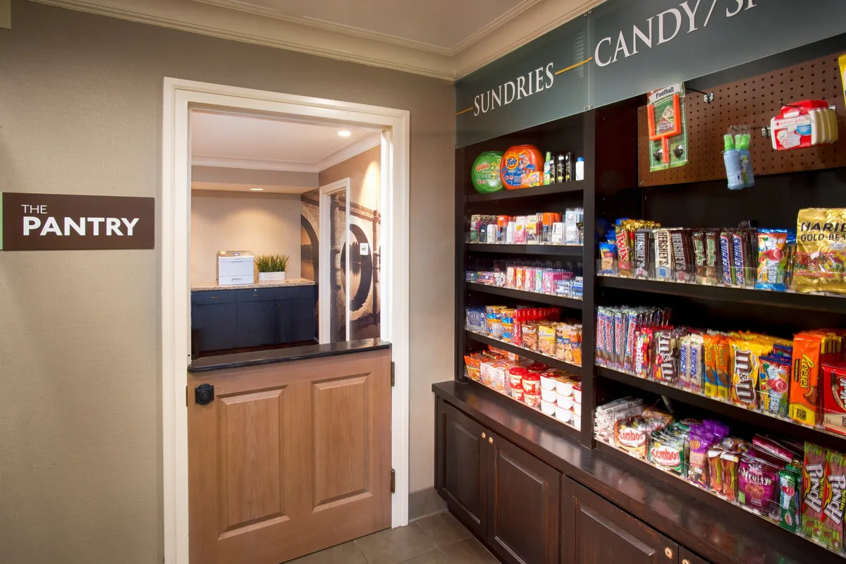 This image shows shelves filled with a variety of snacks in a space labeled 'THE PANTRY.' A doorway leads to another area, inviting guests to explore further. The scene is casual, convenient, and suggests quick access to treats or supplies, perhaps before heading out for local events or seasonal outings.